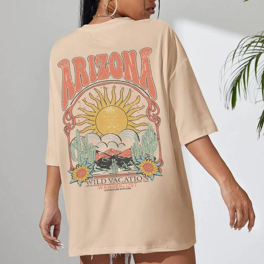 T-shirt Confortable imprimé Soleil ARIZONA porté par une femme avec un mur blanc en fond et une plante verte à droite